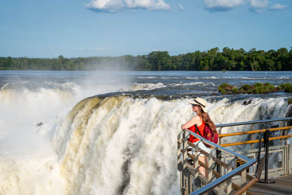 Mujer turista apoyada en la barandilla de una pasarela con vistas a las Cataratas del Iguazú en el lado argentino
