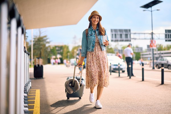 Mujer viajera en las afueras de un aeropuerto con equipaje y documentación en mano.