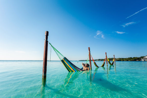 Turista masculino en una hamaca sobre el agua en la Laguna Bacalar del Caribe mexicano en un día soleado.