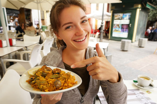 Una mujer sonriente señala un dedo a un plato de paella.