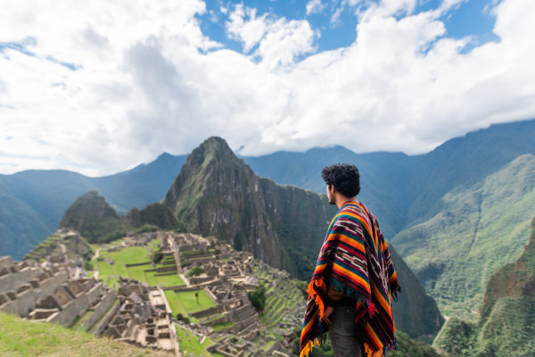 Hombre joven con poncho mirando el Machu Picchu.