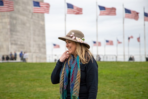 Mujer sonriendo frente al monumento a Washington con banderas estadounidenses de fondo.