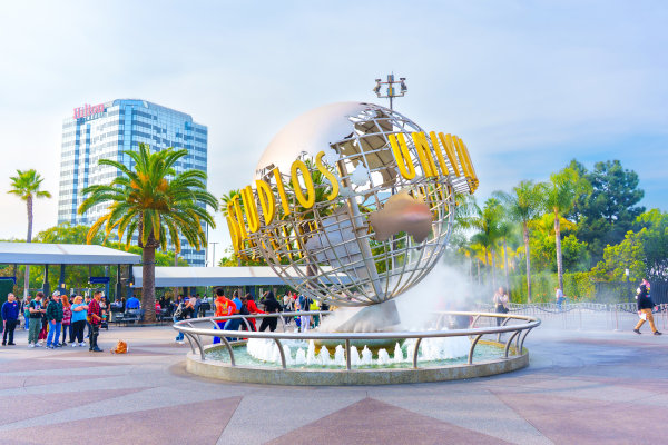 Fuente icónica del globo terráqueo de Universal Studios en la entrada al estudio, llena de visitantes y rodeada de palmeras y edificios en Los Ángeles.