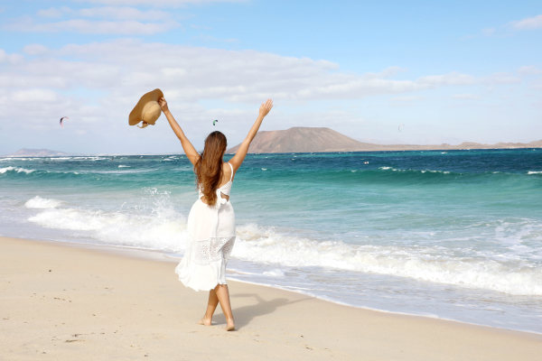Mujer con vestido blanco alzando los brazos en una playa de dunas de Corralejo, Fuerteventura, Islas Canarias.