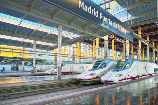 Tren AVE saliendo de la estación de Atocha con destino a Barcelona en un día soleado.