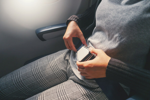 Primer plano de una pasajera femenina ajustándose el cinturón de seguridad en un avión.