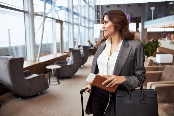 Mujer sonriente con boleto, maleta y bolso en el aeropuerto.