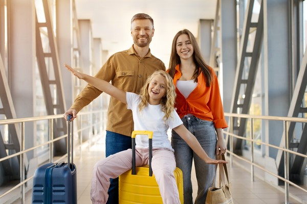 Familia joven posando para una foto en el aeropuerto con sus maletas.
