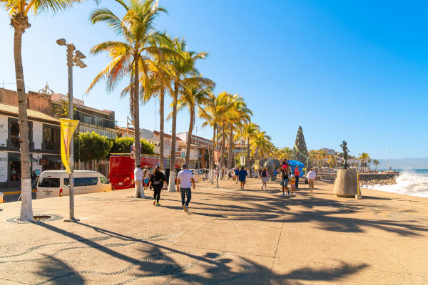 Personas caminando por el malecón lleno de tiendas y cafés a lo largo de la costa de la Bahía de Banderas en la Zona Romántica de Puerto Vallarta, México.