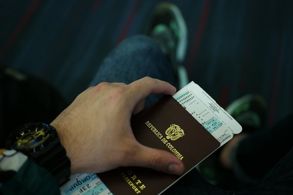 Hombre sentado con pasaporte colombiano y boleto de avión en la mano.