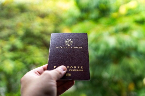 Mano sosteniendo pasaporte colombiano con un fondo verde borroso.