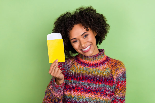 Mujer sonriente con pasaporte en la mano sobre un fondo verde claro liso.
