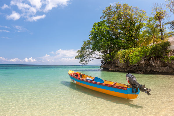 Barco de pescadores azul y amarillo con motor en la orilla de una playa en Jamaica con rocas y vegetación de fondo.