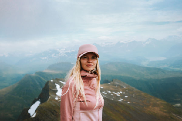 Mujer con gorra y ropa deportiva en la cima de una montaña en Noruega.