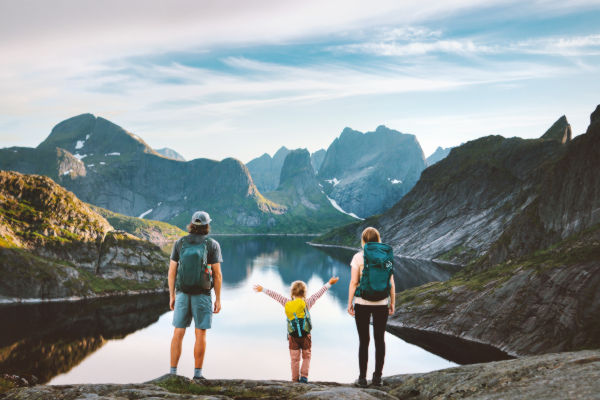 Familia con mochilas observando un lago rodeado de montañas en Noruega.