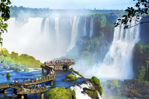 Vista aérea lejana de turistas en una pasarela mirando las Cataratas del Iguazú en un día soleado.