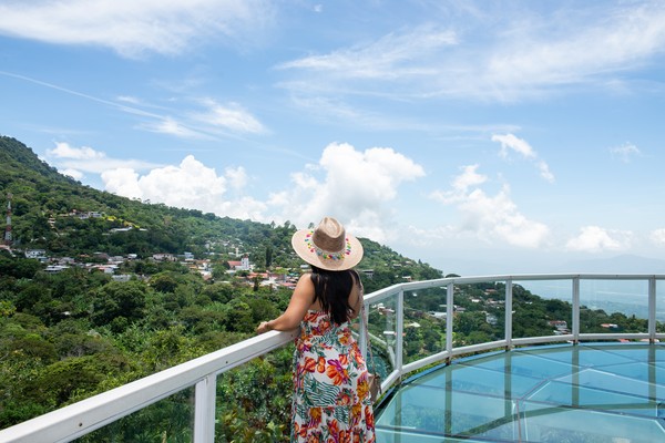 Mujer turista con vestido y sombrero de pie junto a la barandilla de un mirador en San Salvador.