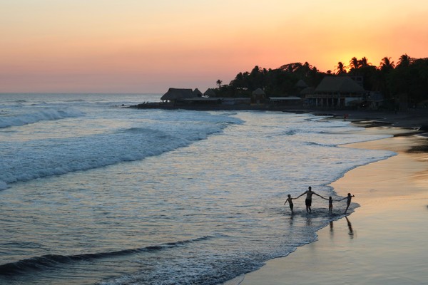 Padre de la mano con sus tres hijos en la orilla de una playa en El Salvador al atardecer.