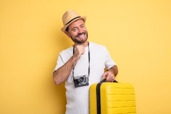 Hombre turista de mediana edad que se siente feliz y tiene una maleta amarilla en mano.