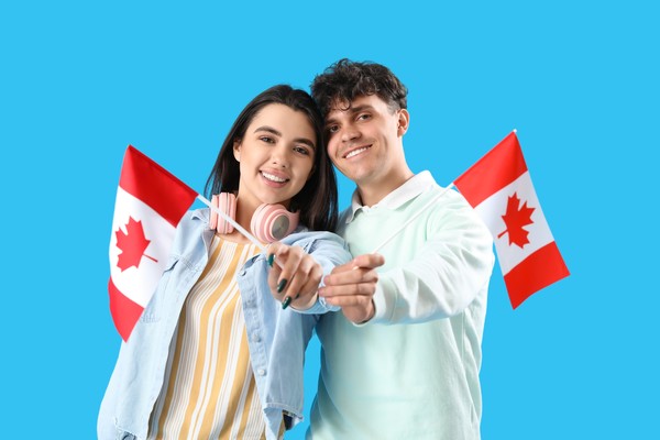 Chico y chica mostrando a cámara banderas de Canadá con fondo liso celeste.