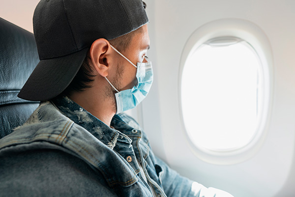 Viajero con mascarilla mirando por la ventanilla de un avión