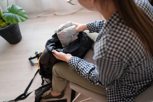 Mujer que prepara su mochila para trekking con ropa y equipamiento adecuados.