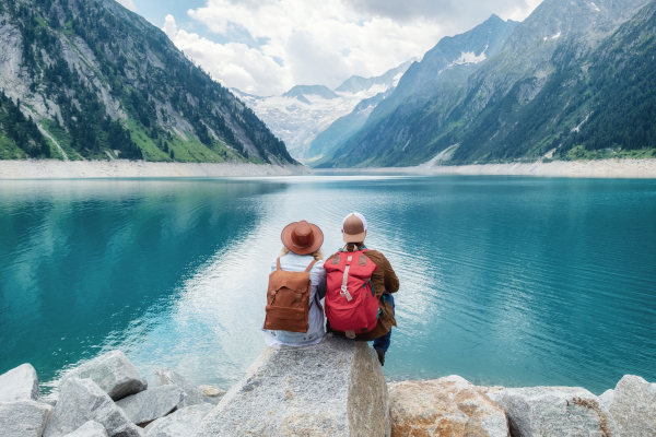 Pareja de viajeros sentados en una roca mirando un lago de montaña en una región montañosa de Austria, Europa.