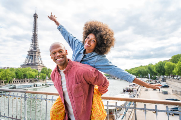 Pareja sonriente posando para una foto en una barandilla de un puente sobre el Río Sena con la Torre Eiffel de fondo