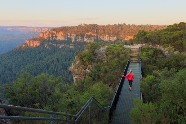 Mujer caminando en un puente de metal para cruzar de una montaña a otra en Australia.