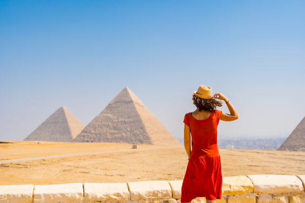 Mujer con sombrero vestida de rojo de espaldas a la cámara mirando las Pirámides de Giza a la distancia