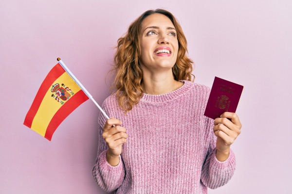 Mujer colombiana que sostiene una bandera española y su reciente visa de trabajo para España