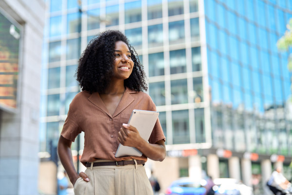 Mujer profesional afrodescendiente, joven y feliz, con una tablet en la mano mientras contempla una ciudad nueva.