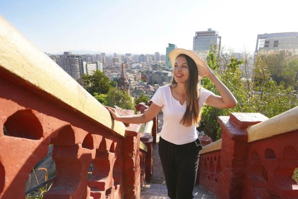 Chica subiendo las escaleras hacia el cerro Santa Lucía en Santiago de Chile durante un día soleado con la ciudad de fondo.