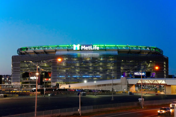 Fachada frontal del MetLife Stadium iluminada al anochecer.