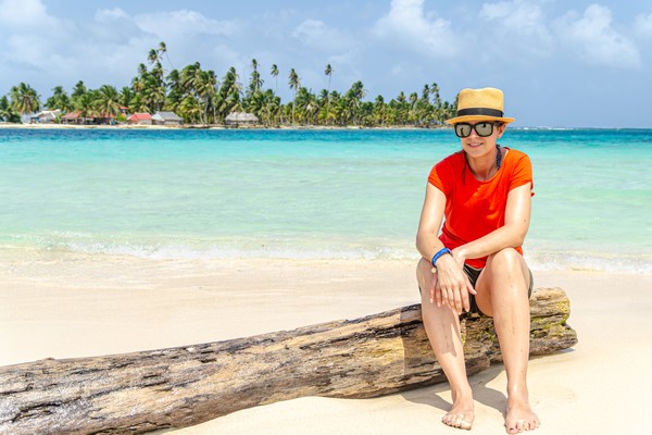 Mujer con camiseta roja sentada en la playa en un tronco de árbol en la isla de San Blas, en Panamá.