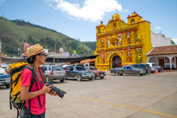 Turista con gran mochila y cámara de fotos profesional frente a una iglesia en una ciudad colonial de Guatemala.