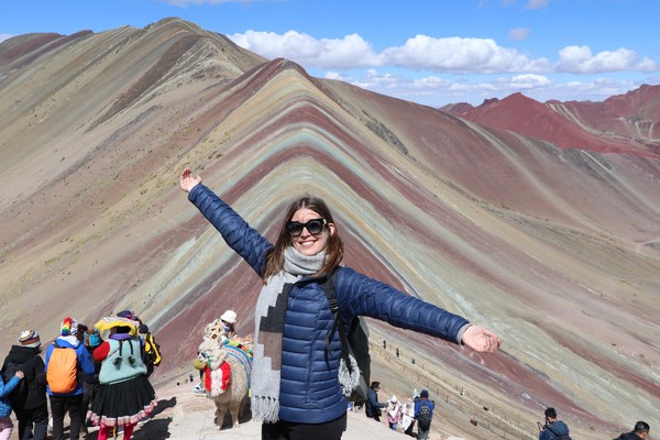 Un turista con los brazos abiertos en la cima de la Montaña Arco Iris, Vinicunca, Perú.