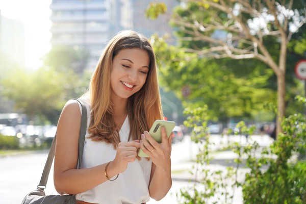 Mujer mirando celular con una sonrisa en un entorno urbano.