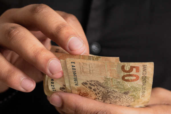Manos de una persona que cuenta billetes de reales en efectivo.