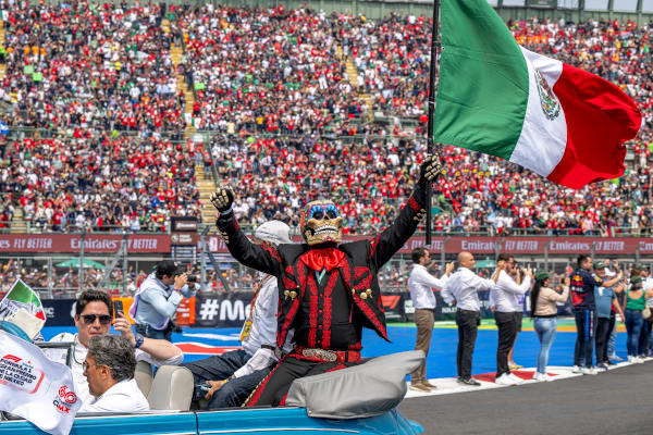 Hombre disfrazado de catrina en la parte trasera de un auto convertible alzando una bandera de México durante el Gran Premio de México de 2022.