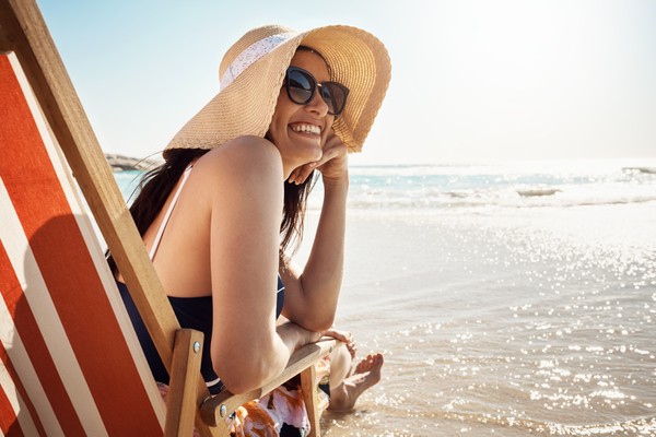 Mujer sonriente con gafas de sol sentada en una reposera rayada en la orilla de una playa en Miami.