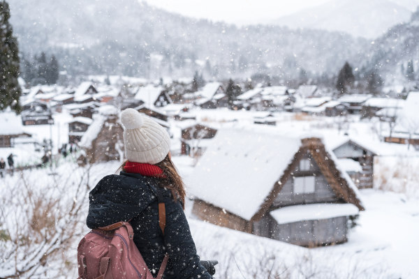 Mujer turista bajo la nieve mirando la villa de Shirakawa en invierno, Japón