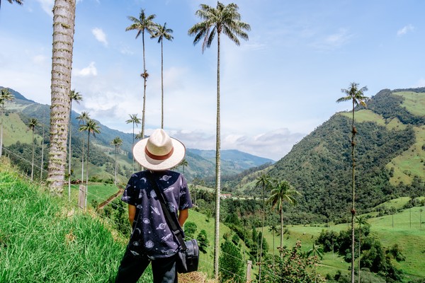 Turista con sombrero y bolso admirando el paisaje en el Valle de Cocora, Colombia.