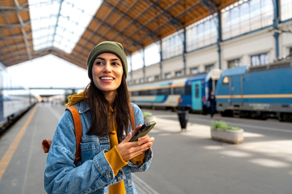 Mujer viajera, en una estación de tren, usando su celular para contactar a su seguro de viajero.