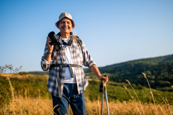Hombre adulto mayor sonriente con cámara y bastón de senderismo.
