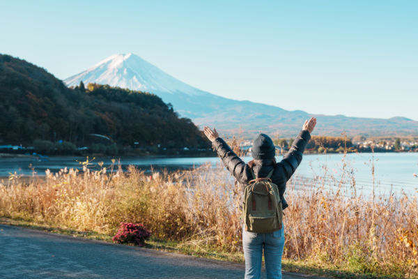 Turista con mochila levantando los brazos frente al Monte Fuji.