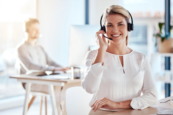 Personal femenino de atención al cliente con auriculares y micrófono sonriendo a cámara.