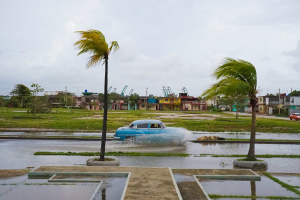 Clásico auto antiguo en la ciudad de Cienfuegos, Cuba, pasando por una calle anegada entre palmeras que se sacuden por el viento del huracán Irma, 2017.