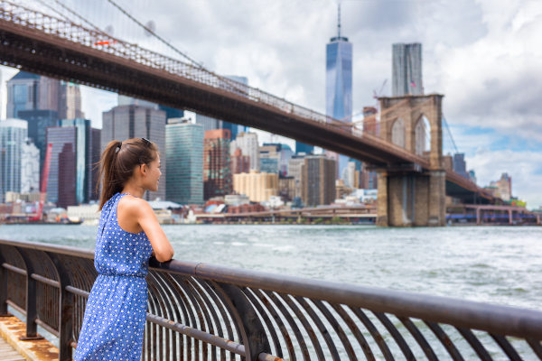 Mujer turista con vestido azul claro disfrutando de las vistas de Manhattan desde el parque de Brooklyn, Nueva York, Estados Unidos.