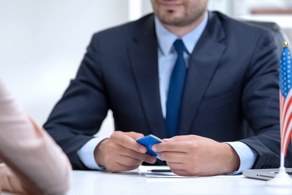 Persona sosteniendo visa americana con pantalla borrosa de fondo.